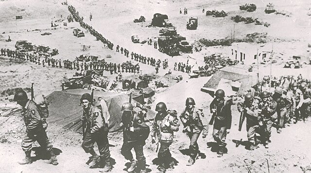 Soldats se déployant en colonnes sur une plage lors du débarquement des forces alliées en Normandie.